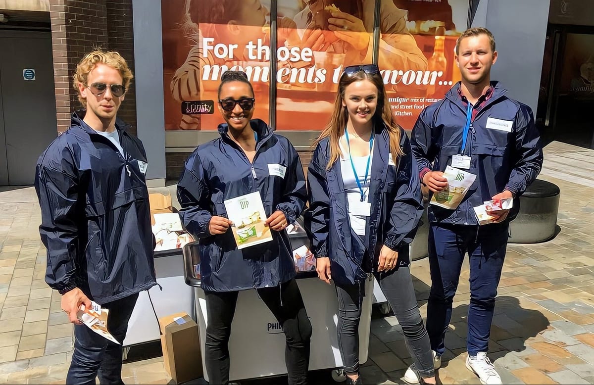 Four Philadelphia sampling team members in navy jackets holding samples and leaflets on a high street