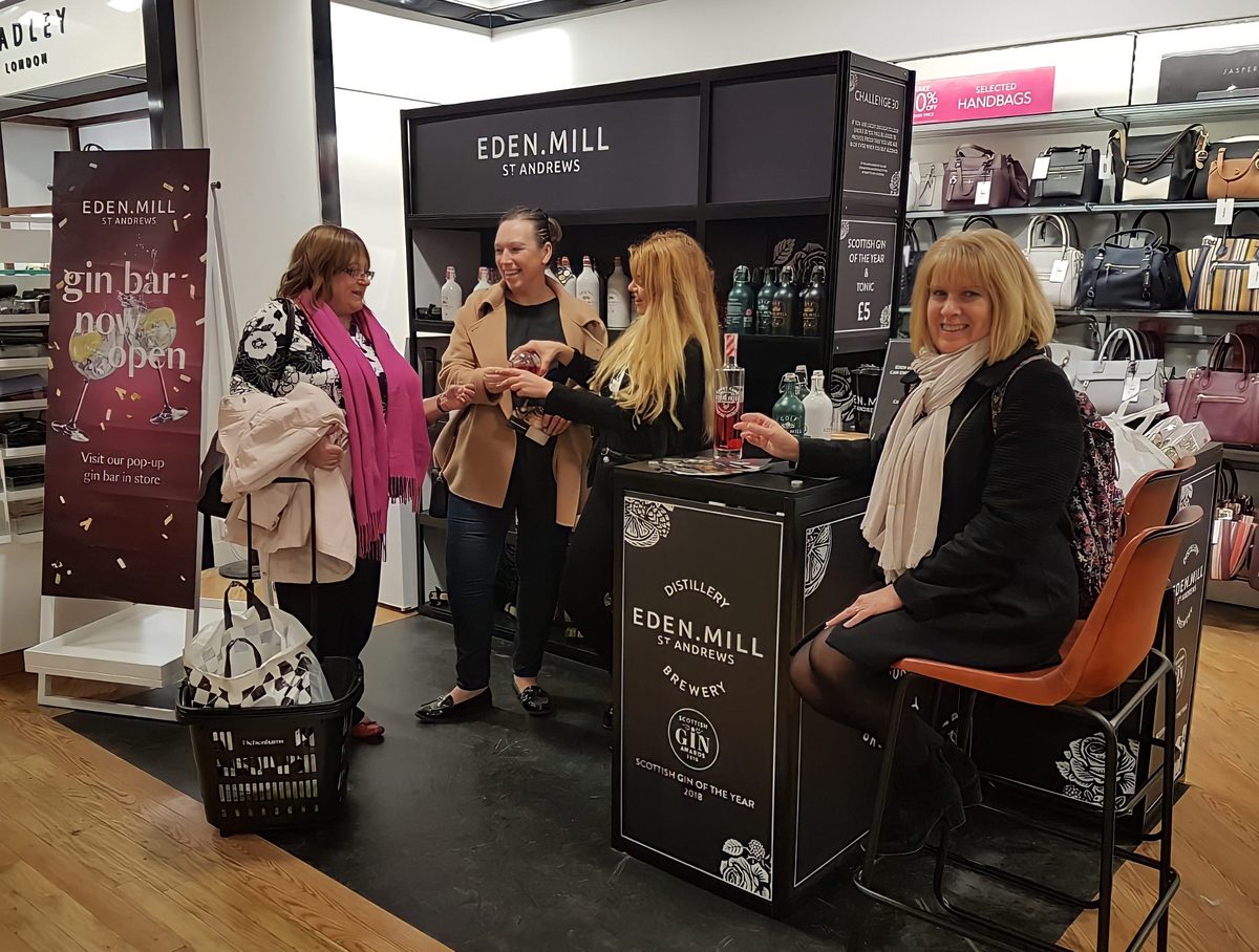 Eden Mill gin bar team serving shoppers at a black branded pop-up bar inside a Debenhams store