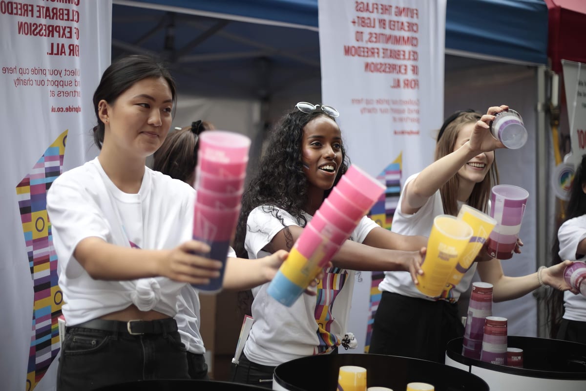 Budweiser brand ambassadors in white Budweiser T-shirts holding up stacks of colourful reusable Pride cups