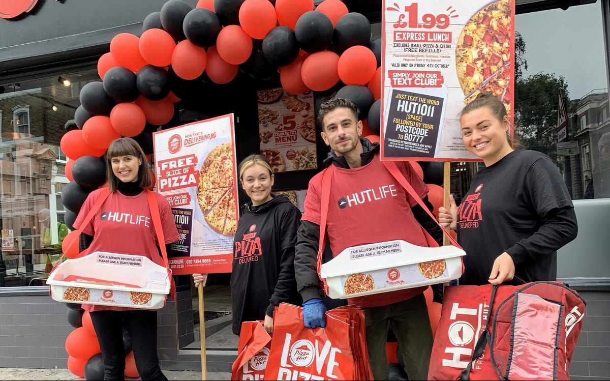 Team in branded clothing holding golf signs at a Pizza Hut opening