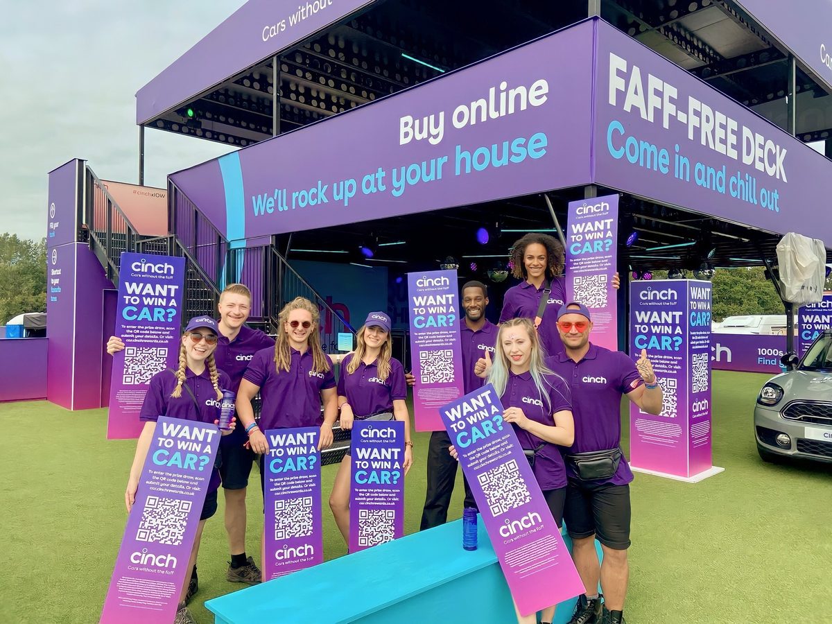 The Cinch festival team in purple uniforms holding competition banners in front of the Faff-Free Deck