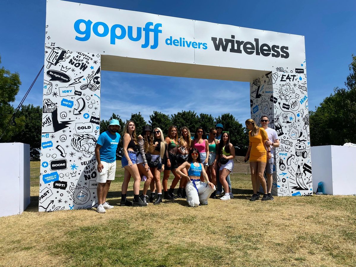 Festival-goers and a team member posing under the illustrated Gopuff Delivers Wireless entrance arch