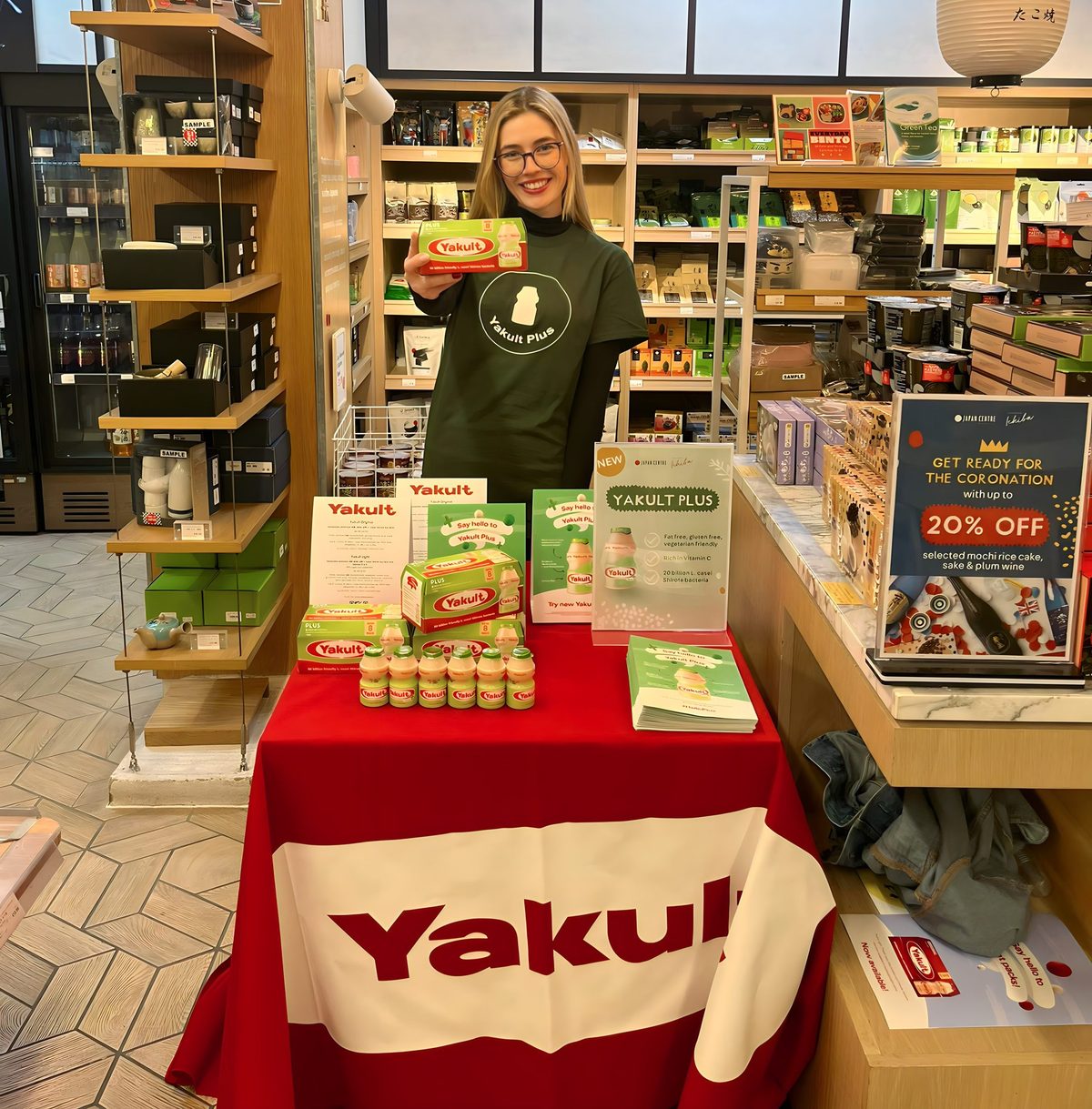 promotional staff in uniforms sampling Yakult+ in a supermarket aisle