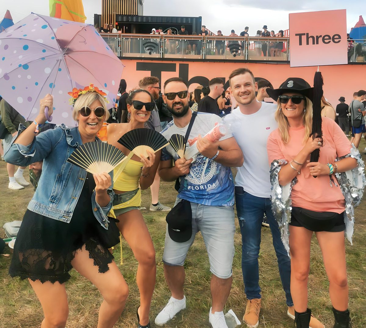 A Three team member with a group of festival-goers holding fans