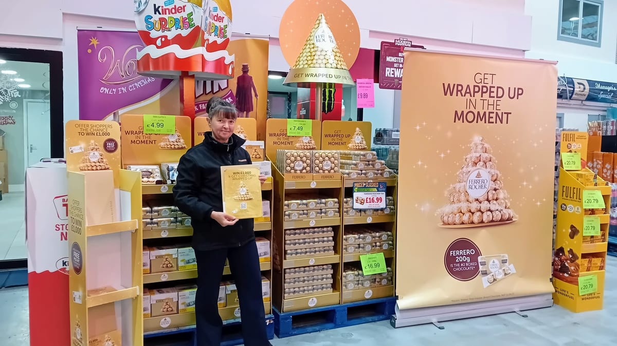 Staff member with a clipboard beside a chocolate display in store