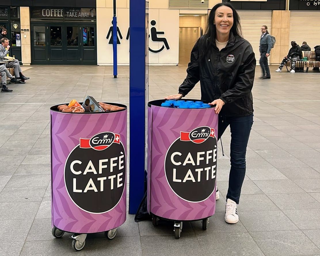 Emmi Caffè Latte sampling team member with branded bins at Leeds train station
