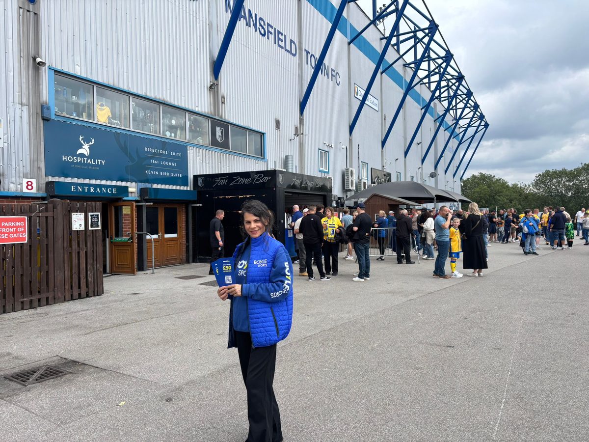 Staff member in a branded jacket with leaflets outside the ground in Mansfield