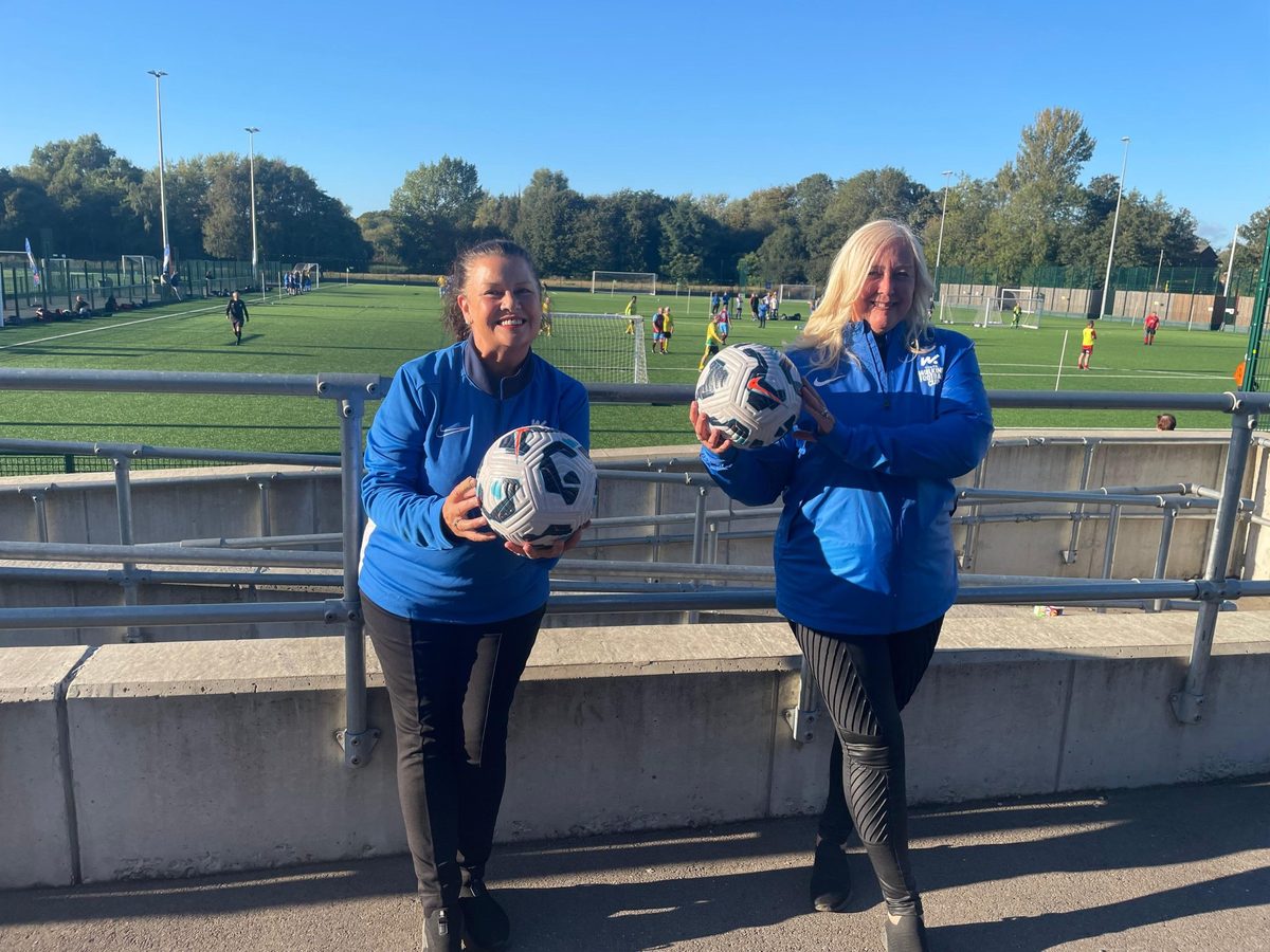 Event support staff in matching blue jackets beside the pitch at a football event