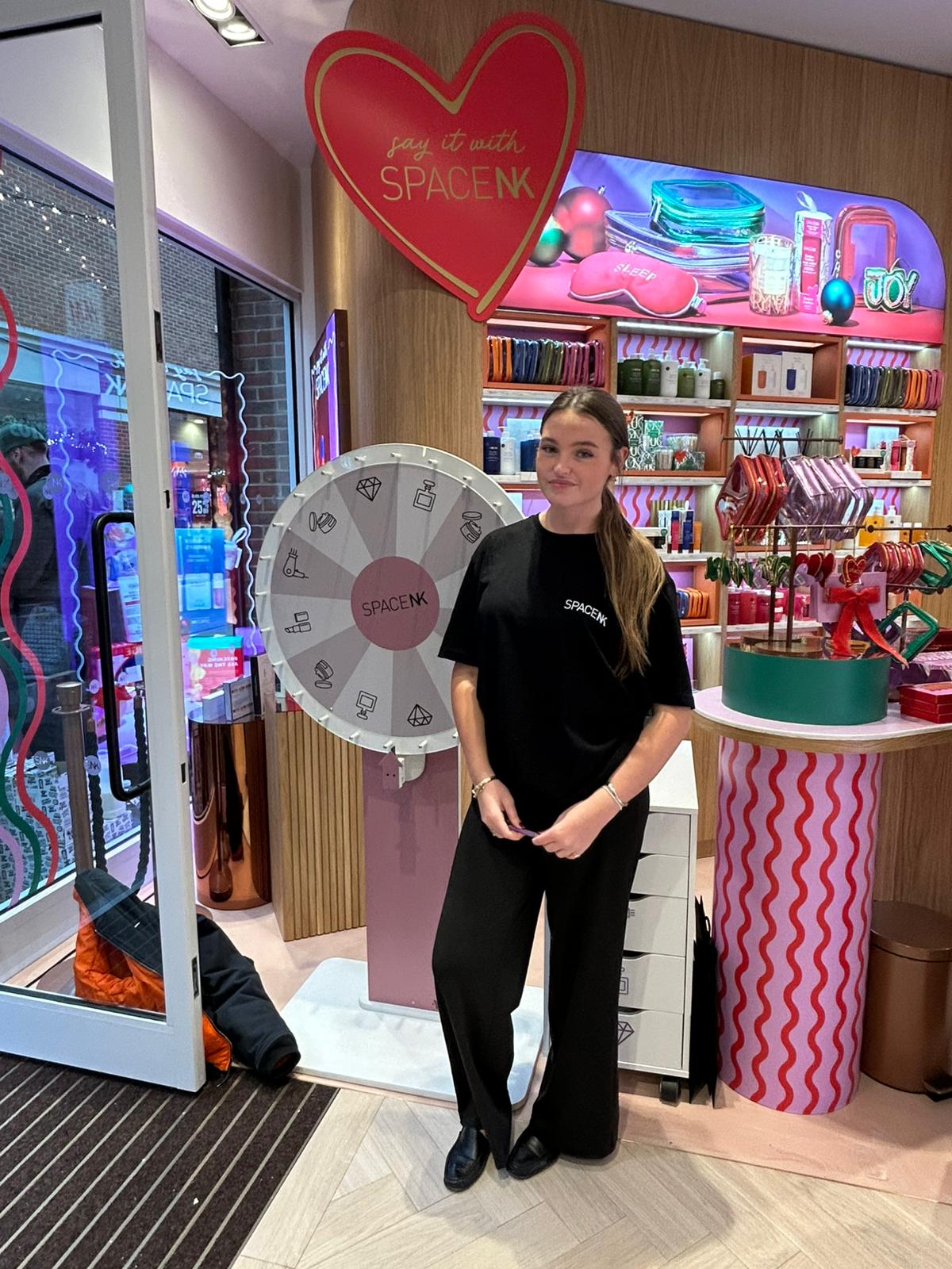 Staff member beside a prize wheel in the Space NK store in Canterbury