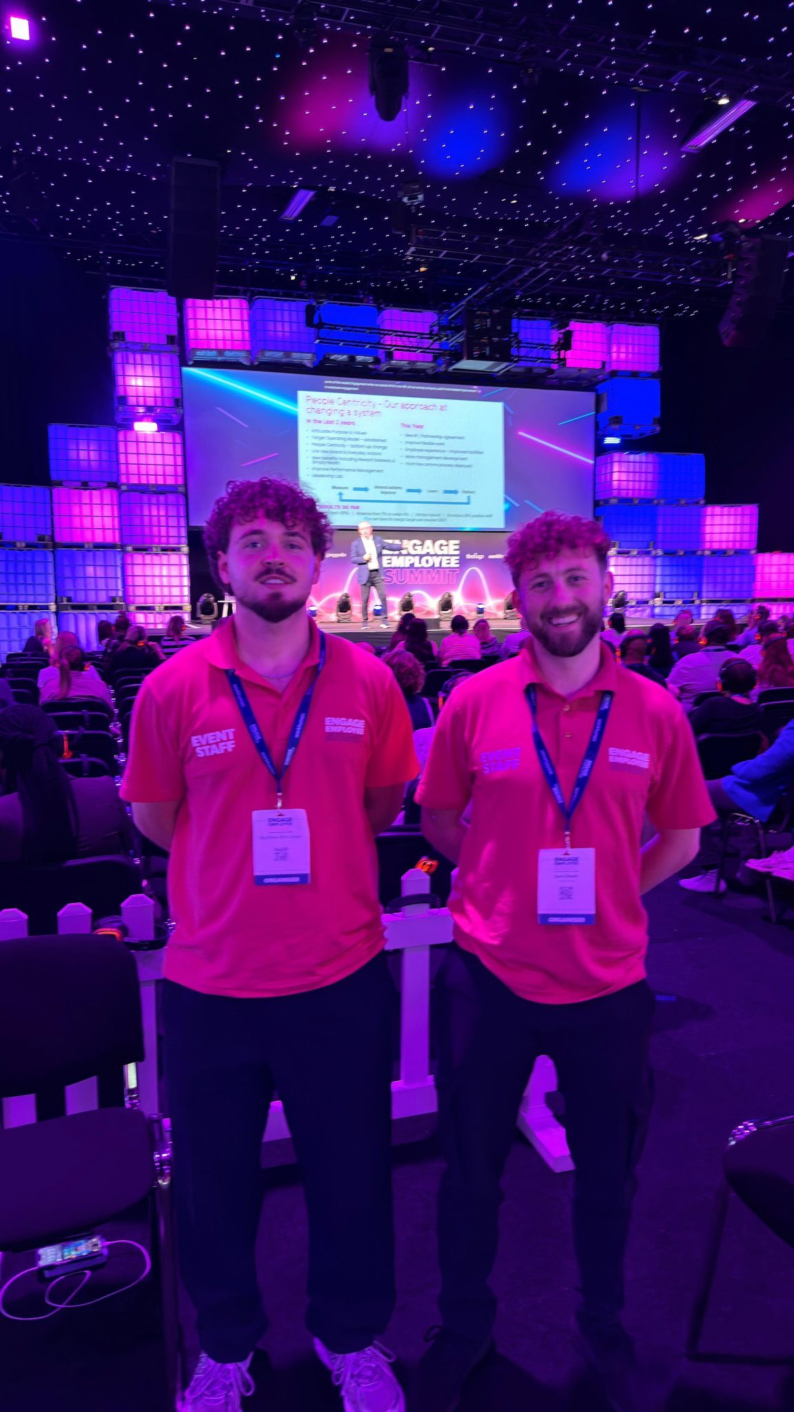 Two conference hosts in matching pink polo shirts and lanyards at the Engage Employee Summit in London
