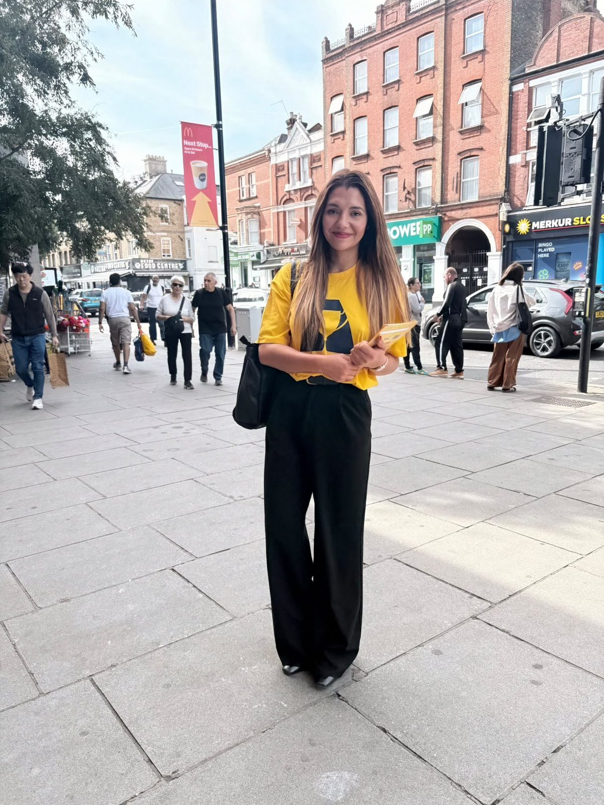 A promotional staff member in a yellow Admiral tee holding flyers on a high street