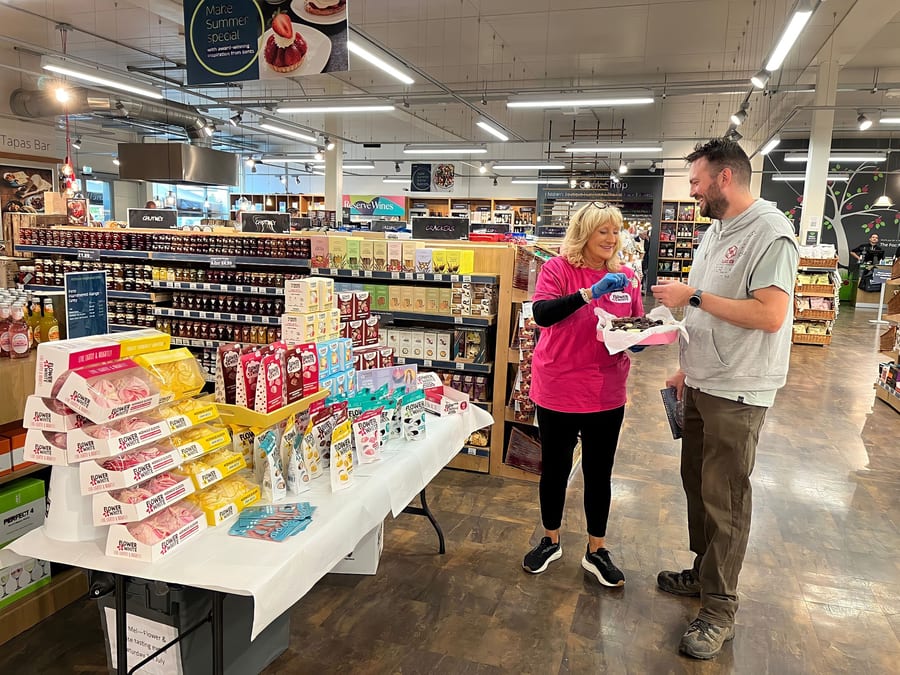 EXECUTIONAL sampler offering a tasting to a shopper beside a supermarket promotion table