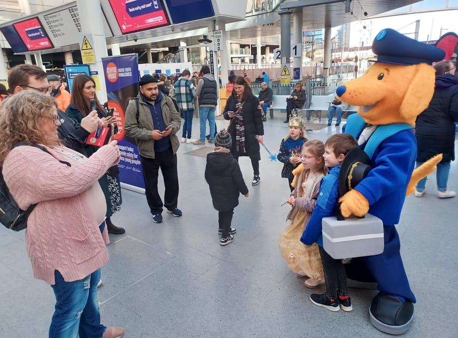 EXECUTIONAL costume character and team meeting families on a Northern station concourse