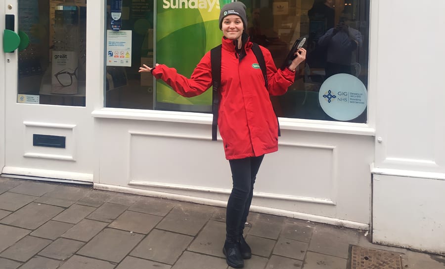 EXECUTIONAL greeter in a red jacket welcoming customers outside a Specsavers store